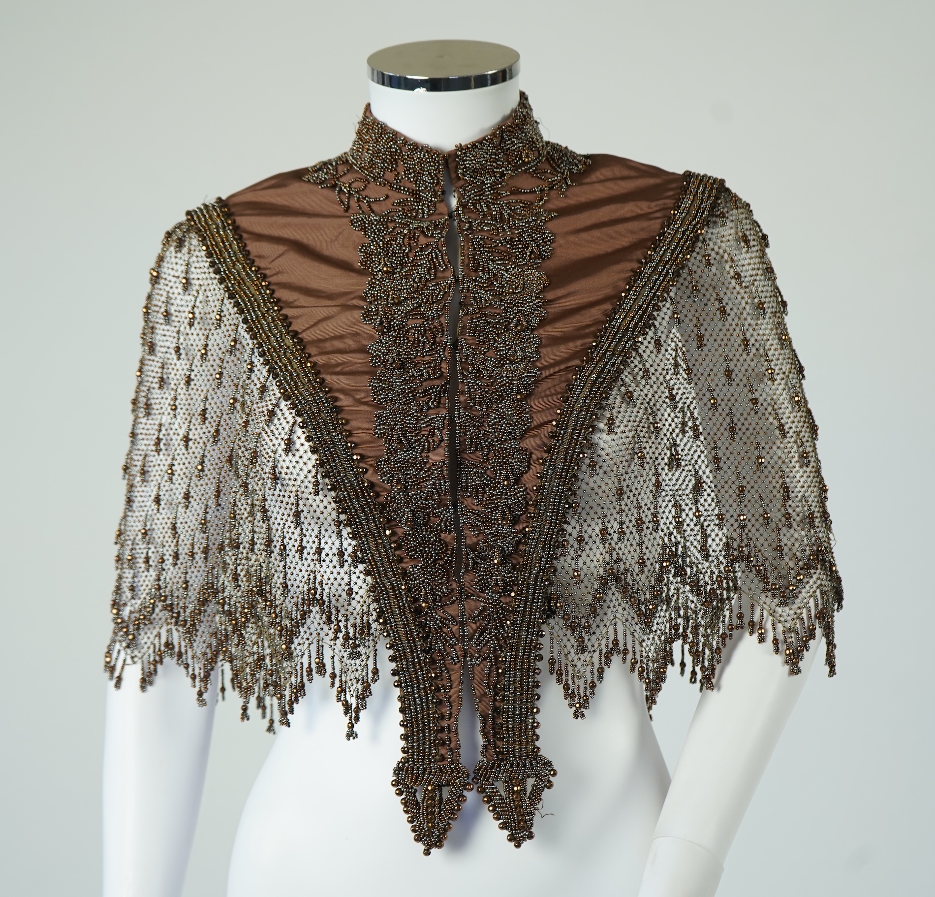 A late 19th century ladies ornate steel and brown beaded and fringed shoulder cape. Made as three ribbed silk panels with ornate beaded appliqués with a beaded and fringed net sleeved cape. Top of neck to bottom of beadi
